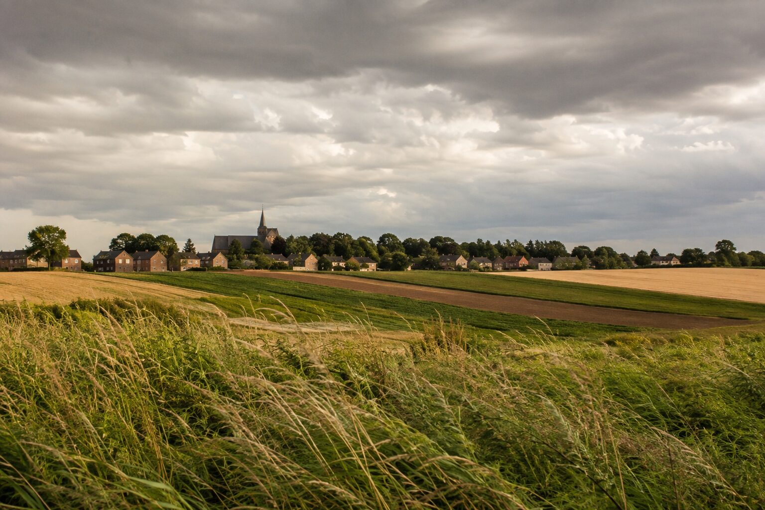 Een zware bewolkte lucht boven een Limburgs dorp met glooiende akkers eronder